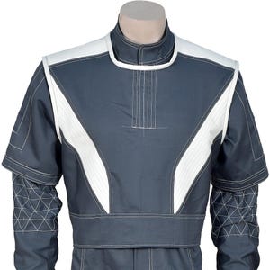 May include: A dark gray jumpsuit with white accents. The jumpsuit features white panels on the shoulders and chest, outlined with white stitching. The sleeves have geometric patterns, and the collar is a stand-up style.