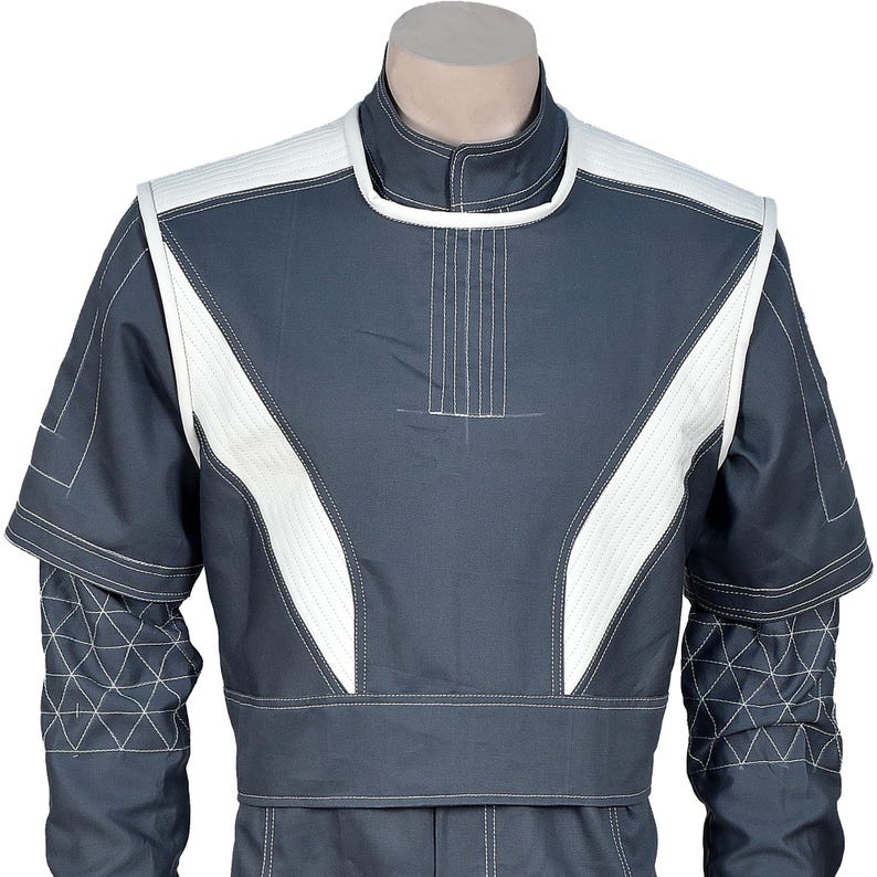 May include: A dark gray jumpsuit with white accents. The jumpsuit features white panels on the shoulders and chest, outlined with white stitching. The sleeves have geometric patterns, and the collar is a stand-up style.