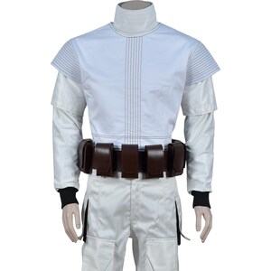 May include: White costume with a high collar, long sleeves, and a brown belt with pouches. The top has vertical stitching and short sleeves. The pants are white with a side pocket. Black cuffs are visible at the wrists.