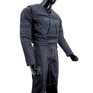 May include: Black tactical jacket and pants set. The jacket features a quilted design on the shoulders and chest, with white stitching outlining the panels and geometric patterns on the sleeves. The pants have white stitching along the seams.