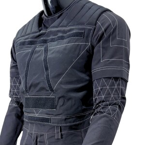 May include: Black quilted jacket with white stitching and velcro closures. The jacket features a geometric design on the sleeves and chest. The garment is displayed on a mannequin.
