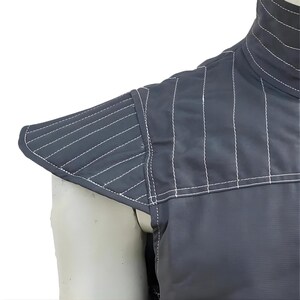 Op de afbeelding: Close-up van een donkergrijs kledingstuk met witte stiksels. Het kledingstuk heeft een hoge kraag en gewatteerde schouderdetails. De stiksels cre&euml;ren een gewatteerd effect op de schouder en kraag.