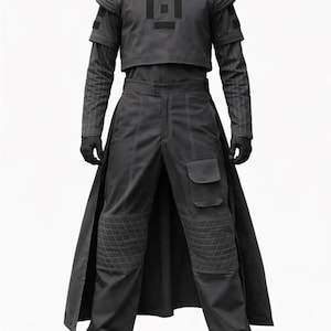 K&ouml;nnte beinhalten: Ein dunkelgraues futuristisches Outfit mit einem bauchfreien Oberteil mit geometrischem Design, einer lang&auml;rmeligen Unterschicht und einer hoch taillierten Hose mit gesteppten Knieschonern und Cargotaschen. Das Outfit umfasst einen langen, flie&szlig;enden Rock und schwarze Handschuhe.