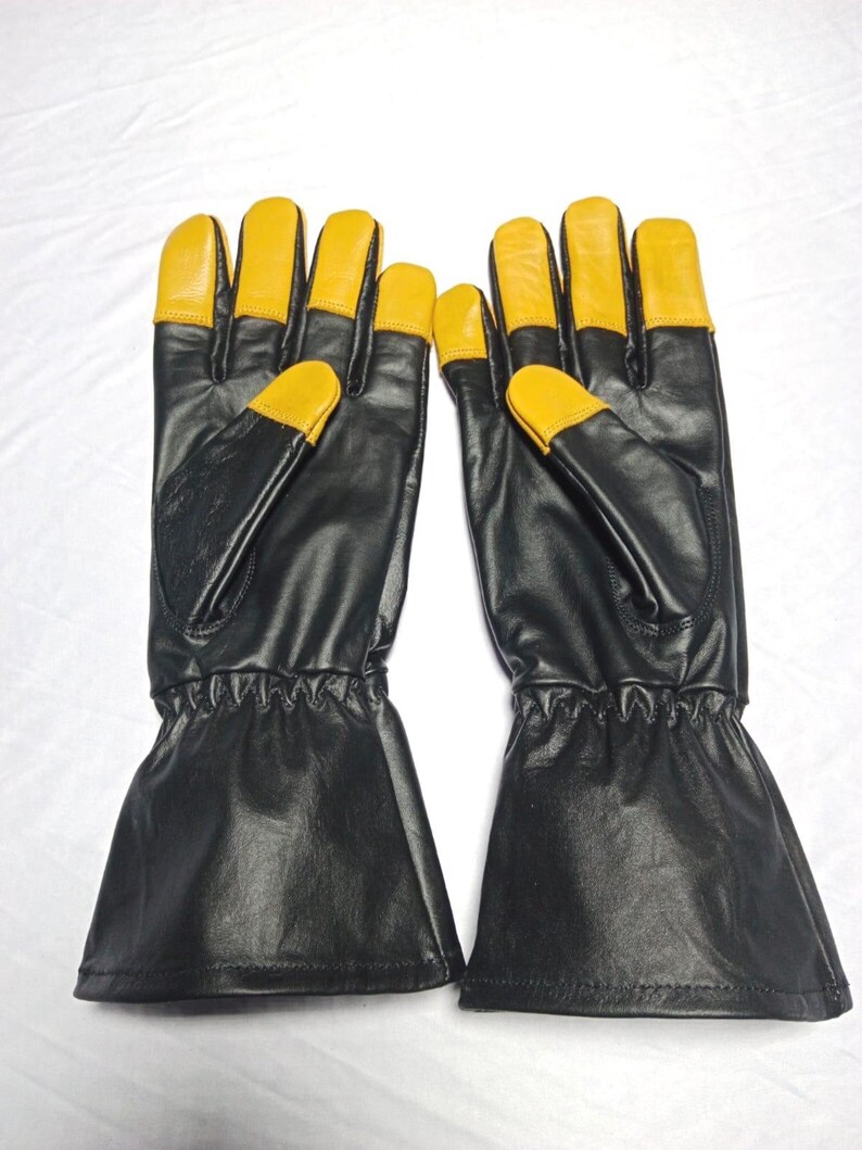 May include: A pair of black leather gloves featuring long cuffs and contrasting yellow leather fingertips. The gloves have a smooth finish, stitched seams, and a gathered elastic wrist section to ensure a secure fit during use.