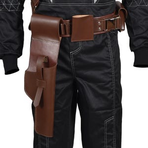 May include: A brown leather holster and belt set. The holster is designed to hold a pistol and is attached to a brown leather belt with a silver buckle. The belt also features a small pouch. The person is wearing black pants and a black jacket.