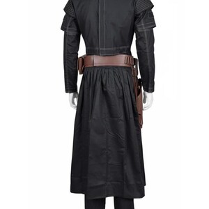May include: Black costume with a long skirt, long-sleeved jacket, and brown belt. The jacket has white stitching and shoulder accents. A brown holster is attached to the belt. The costume is displayed on a mannequin.