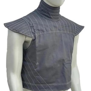 Op de afbeelding: Een grijze vest met een hoge kraag en schoudervullingen. De vest is gemaakt van een gewatteerd materiaal met witte stiksels. Het ontwerp omvat verticale en diagonale lijnen, waardoor een gestructureerd uiterlijk ontstaat. De vest wordt op een mannequin getoond.
