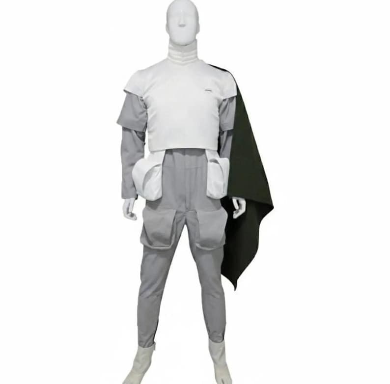 May include: A futuristic costume displayed on a mannequin. The outfit includes a white top, gray pants with pockets, and a dark green cape. The mannequin wears white boots. The costume is designed with a high collar.