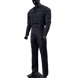 May include: Black jumpsuit with white stitching details. The top features a quilted design on the shoulders and chest, with long sleeves. The pants are straight-legged. The outfit is displayed on a black mannequin.
