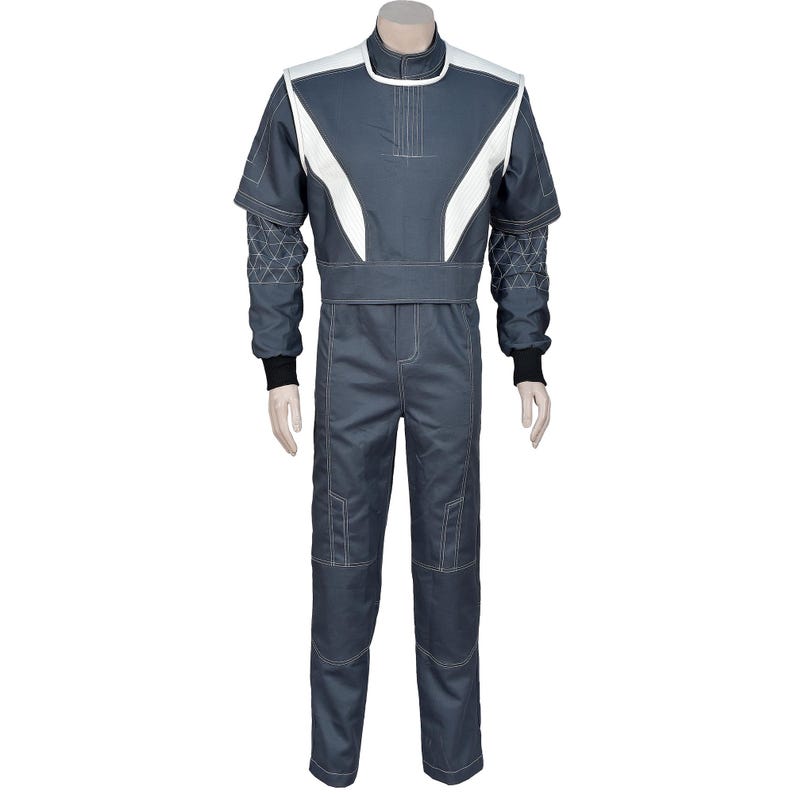 May include: A gray racing suit with white accents on the shoulders and chest. The suit has a high collar, long sleeves, and a fitted waist. Black cuffs and white stitching detail the suit. The suit is displayed on a mannequin.
