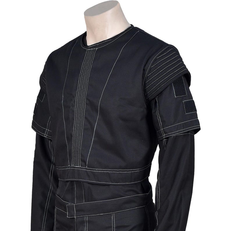 May include: Black jumpsuit with white stitching details. The garment features a round neck, long sleeves, and a fitted waist. The shoulders have layered accents with square patches. The design includes vertical and horizontal stitching patterns.