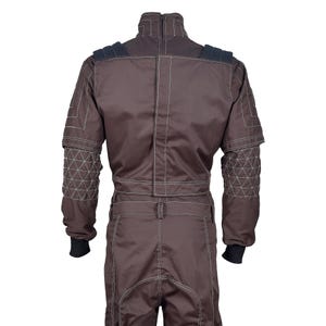 Puede incluir: Mono de carreras marr&oacute;n con costuras blancas y detalles negros. El mono tiene cuello alto, hombreras y detalles geom&eacute;tricos en las mangas. Cuenta con cierre de cremallera y est&aacute; dise&ntilde;ado para deportes de motor.