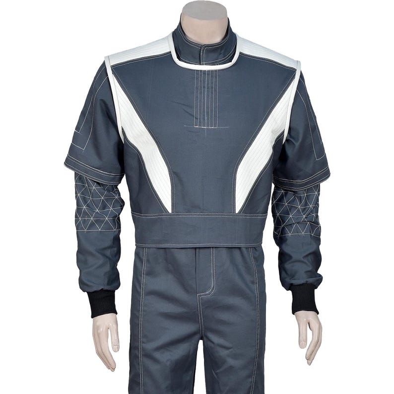 May include: A dark gray racing suit with white accents on the shoulders and chest. The suit features geometric stitching on the sleeves and a black cuff at the wrist. The suit is designed for motorsports.