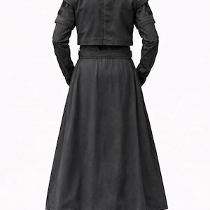 K&ouml;nnte beinhalten: Ein schwarzes Outfit mit einer kurzen Jacke mit strukturierten Schultern und langen &Auml;rmeln, einem breiten G&uuml;rtel, einem langen Rock und einer passenden Hose. Die Jacke hat einen hohen Ausschnitt und der Rock ist bodenlang. Das Outfit ist aus einem dunklen, m&ouml;glicherweise strukturierten Stoff.