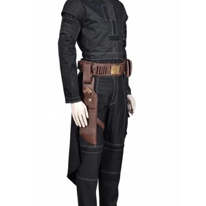 May include: Black costume with white stitching details. The outfit includes a long-sleeved top, pants, and a brown leather belt with a holster. The top has a round neck and padded shoulders. The costume is displayed on a mannequin.