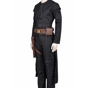 May include: Black costume with white stitching details, featuring a long-sleeved top and pants. The outfit includes a brown belt with pouches and a holster. The pants have padded knee sections. A mannequin displays the complete ensemble.