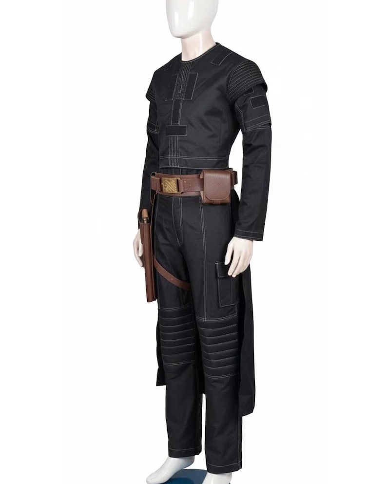 May include: Black costume with white stitching details, featuring a long-sleeved top and pants. The outfit includes a brown belt with pouches and a holster. The pants have padded knee sections. A mannequin displays the complete ensemble.