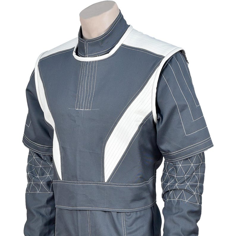 May include: A gray jumpsuit with white accents on the shoulders and chest. The jumpsuit features geometric stitching on the sleeves and a high collar. The design includes a white stripe down the front and white shoulder pads.