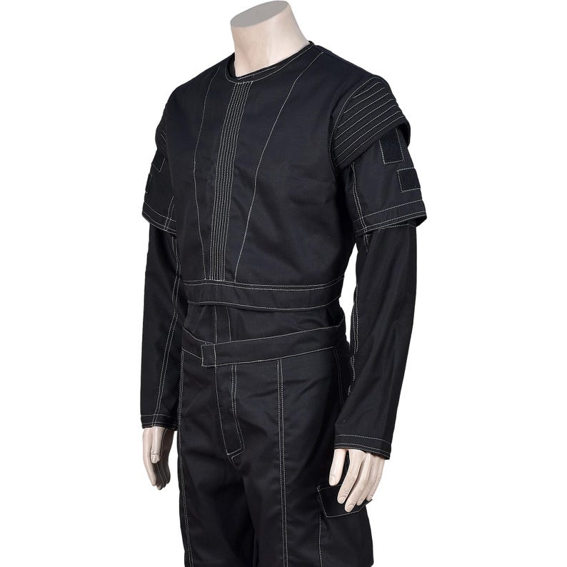 May include: Black jumpsuit with white stitching details. The garment features long sleeves, a round neckline, and a structured design with visible seams and panels. The jumpsuit has a utilitarian aesthetic, with a tailored fit and a mock neck.
