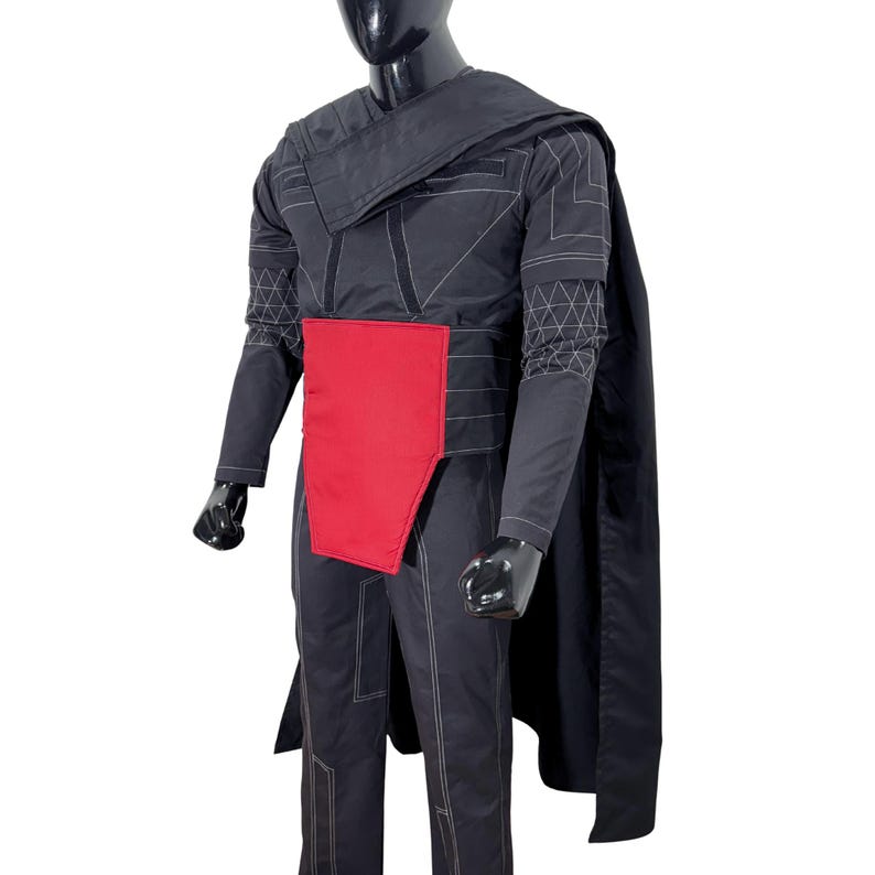 Puede incluir: Traje negro con un panel rojo y capa. El atuendo presenta costuras geom&eacute;tricas y un cuello alto. El maniqu&iacute; lleva guantes negros. El disfraz es probablemente para cosplay o un evento tem&aacute;tico.