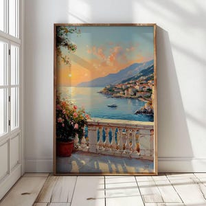 May include: A framed vertical wall art print depicting a coastal Mediterranean scene at sunset. The view features a stone balustrade, a potted plant with pink flowers, a calm blue sea, a small boat, and a hillside town under a golden sky.