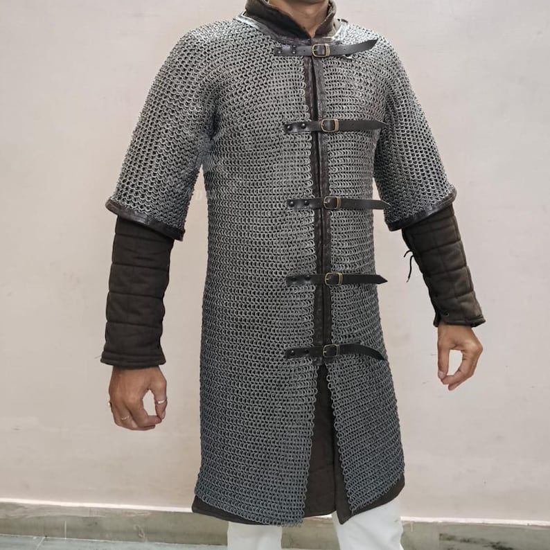 May include: A silver chainmail shirt with short sleeves and a leather collar. The shirt has leather straps with buckles down the front and dark brown padded sleeves. The garment is designed for historical reenactment or costume use.
