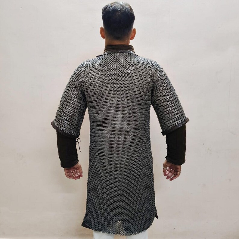 May include: A silver chainmail shirt with short sleeves and a long tunic design. The shirt has a dark brown collar and cuffs, and is worn over a black long-sleeved shirt. The chainmail has a pattern on the back.