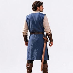 May include: A blue sleeveless tunic worn over a beige long-sleeved shirt, paired with brown leather arm bracers, a brown leather belt, and brown leather boots. A wooden sword in a brown leather scabbard hangs from the belt at the waist.