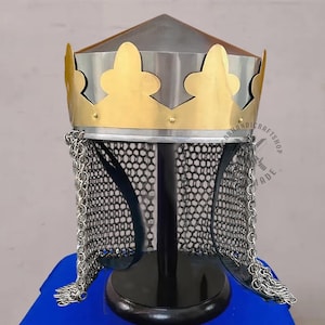 Può includere: Un elmo in stile medievale con una corona dorata e cotta di maglia. L'elmo ha una parte superiore argentata e un supporto nero. La corona presenta ritagli decorativi. La cotta di maglia pende dalla base dell'elmo.