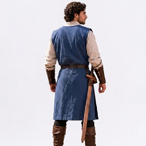May include: A blue sleeveless tunic worn over a beige long-sleeved shirt, paired with brown leather arm bracers, a brown leather belt, and brown leather boots. A wooden sword in a brown leather scabbard hangs from the belt at the waist.
