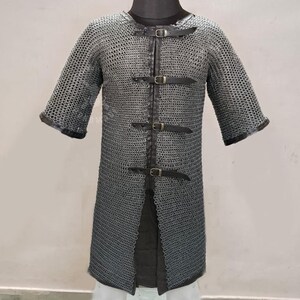 May include: A chainmail shirt with short sleeves, featuring a metal mesh design. The shirt has a front opening secured by three leather straps with buckles. The sleeves and neckline are trimmed with dark leather.