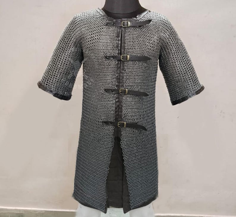 May include: A chainmail shirt with short sleeves, featuring a metal mesh design. The shirt has a front opening secured by three leather straps with buckles. The sleeves and neckline are trimmed with dark leather.