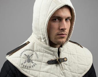 May include: An off-white quilted hood with a matching shoulder mantle, featuring vertical and diamond-shaped stitching patterns. The garment includes dark brown leather straps with brass-toned metal buckles for closure and adjustment.