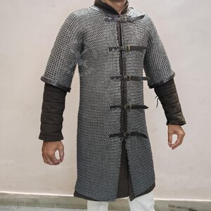 May include: A silver chainmail shirt with short sleeves and a leather collar. The shirt has leather straps with buckles down the front and dark brown padded sleeves. The garment is designed for historical reenactment or costume use.