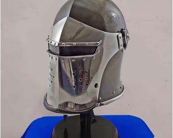 Peut inclure: Casque de chevalier en acier poli avec une visière percée de petits trous d'aération. Le casque a un sommet arrondi et est monté sur un support noir. La visière comporte une section en maille pour la visibilité et la protection. Réplique historique.