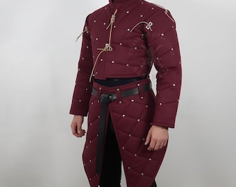 May include: Burgundy quilted medieval doublet and skirt set with silver-colored studs. The high-collared jacket has long sleeves and leather ties. The skirt has a wrap-around design and a black belt.