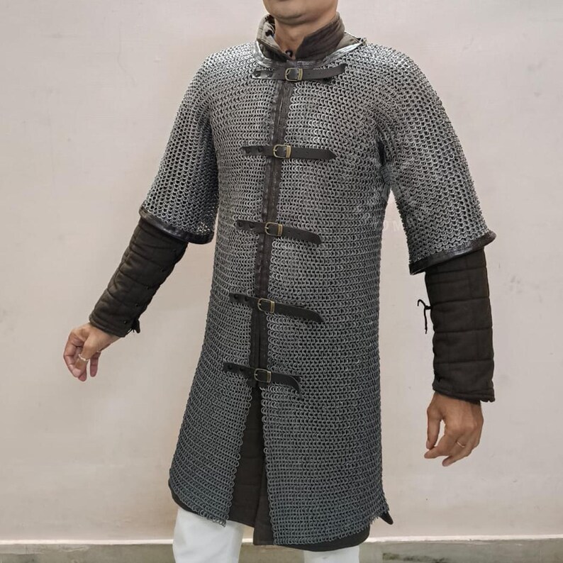 May include: A silver chainmail shirt with short sleeves and a leather-strapped front closure. The shirt has a long, tunic-like design and is worn over padded sleeves. The overall aesthetic is reminiscent of medieval armor.