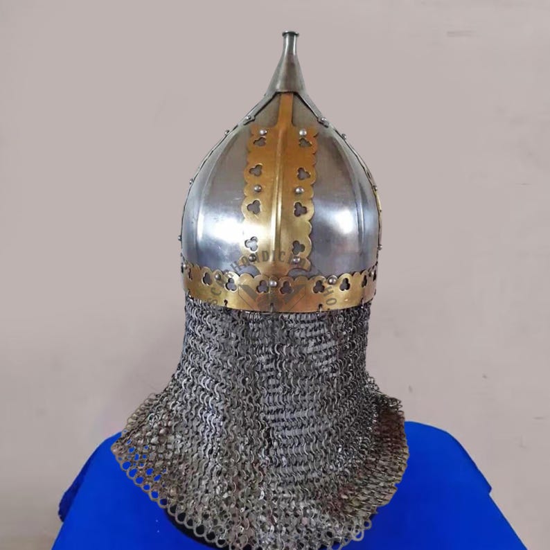 May include: A silver and gold medieval helmet with a chainmail neck guard. The helmet features a pointed top and decorative gold accents along the crown and face. The chainmail extends down to the shoulders.