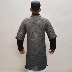 May include: A silver chainmail shirt with short sleeves and a long tunic design. The shirt has a dark brown collar and cuffs, and is worn over a black long-sleeved shirt. The chainmail has a pattern on the back.