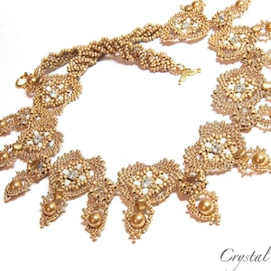 May include: A gold beaded necklace with a delicate, intricate design. The necklace features a central pendant with a floral motif and cascading drops of beads. The necklace is labeled 'Valentina' Necklace.