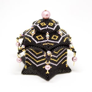May include: A black and gold beaded box with a pink lid and dangling pink beads. The box is shaped like a star and has a geometric pattern.