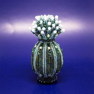 May include: A beaded vase with a green and blue iridescent finish and a white beaded top. The vase is shaped like a bulb with a rounded bottom.