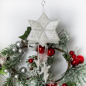May include: A white beaded star ornament with red and silver ornaments on a green and white artificial Christmas tree branch.