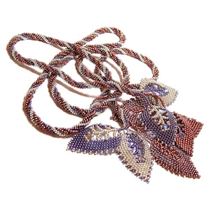 May include: A silver and brown beaded necklace with a decorative pendant featuring a flower design. The pendant is made of purple, silver, and brown beads.