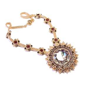 May include: A gold beaded necklace with a large crystal pendant. The pendant is surrounded by smaller beads in gold and purple.