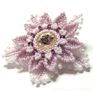 May include: A delicate flower-shaped brooch made of pink and white beads with a clear crystal in the center. The brooch is surrounded by smaller purple beads.