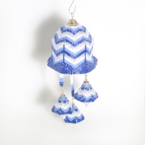 May include: A blue and white beaded ornament with a chevron pattern. The ornament is shaped like a bell and has four smaller bells hanging from it.