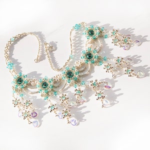 Op de afbeelding: Een zilveren en turquoise kralenketting met meerdere strengen en hangende bedels. De ketting heeft een centraal ontwerp van turquoise en zilveren kralen, met kleinere turquoise kralen en zilveren accenten over de hele lengte.