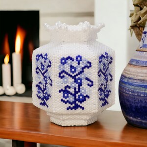 May include: A white ceramic vase with a blue and white floral pattern. The vase is decorated with white beads around the top.