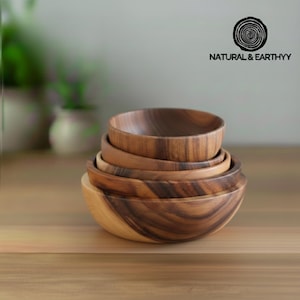 Könnte beinhalten: Ein Stapel von fünf Holzschalen in verschiedenen Größen, die natürliche Holzmaserungsmuster aufweisen. Die Schalen sind auf einer hellen Holzoberfläche angeordnet. Das Logo "NATURAL & EARTHYY" ist sichtbar.